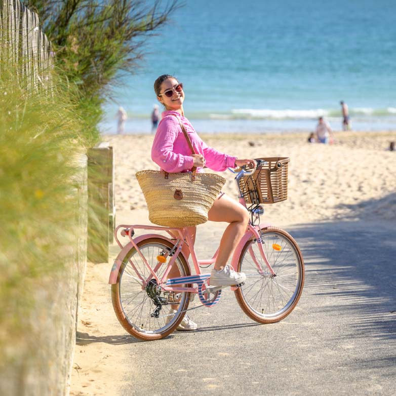 Jeune femme en rose sur un vélo à l'entrée d'une plage à Oléron